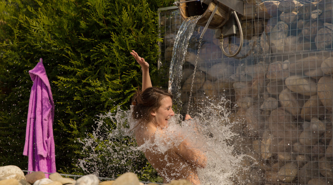 Vrouw staat in de zomer onder een stortemmer met koud water