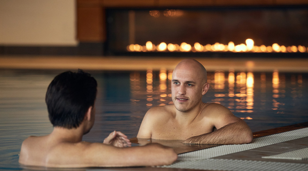 Twee mannen in warm binnenzwembad met open haard op de achtergrond